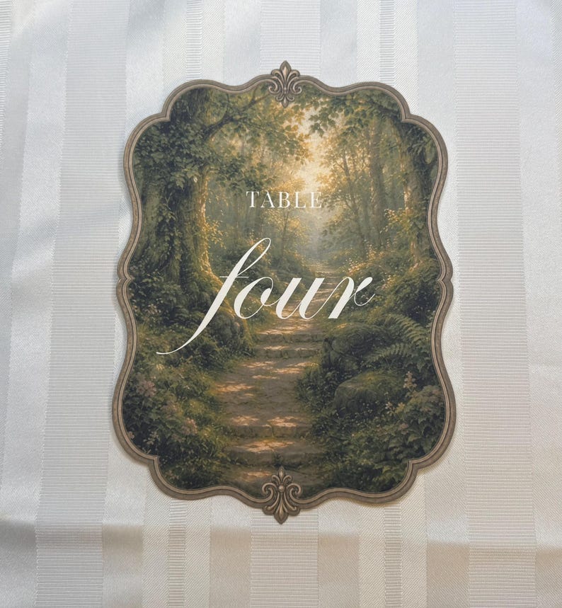 May include: A scalloped-edge table sign featuring a printed forest path scene with green trees and sunlight. The text "TABLE" appears in a small serif font above the large, white, cursive script word "four" centered on the card.
