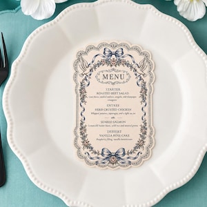 May include: A white scalloped-edge plate with a menu card, fork, and knife. The menu card has a floral and ribbon design with the word "MENU" at the top. The menu lists a starter, entree, and dessert.