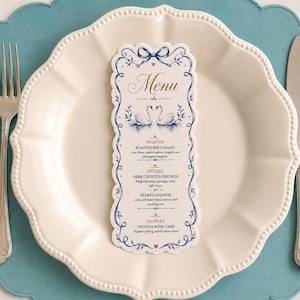 May include: A formal place setting featuring a white scalloped plate, a menu card, a fork, and a knife. The menu card has a blue and gold design with the word "Menu" at the top and a swan illustration.