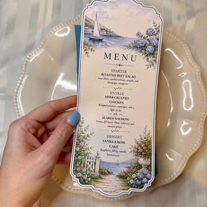 May include: A tall, scalloped-edge menu card featuring a coastal illustration with a sailboat, blue hydrangeas, and a garden path. The text lists a starter of roasted beet salad, entrees of herb crusted chicken or seared salmon, and a vanilla rose cake dessert.