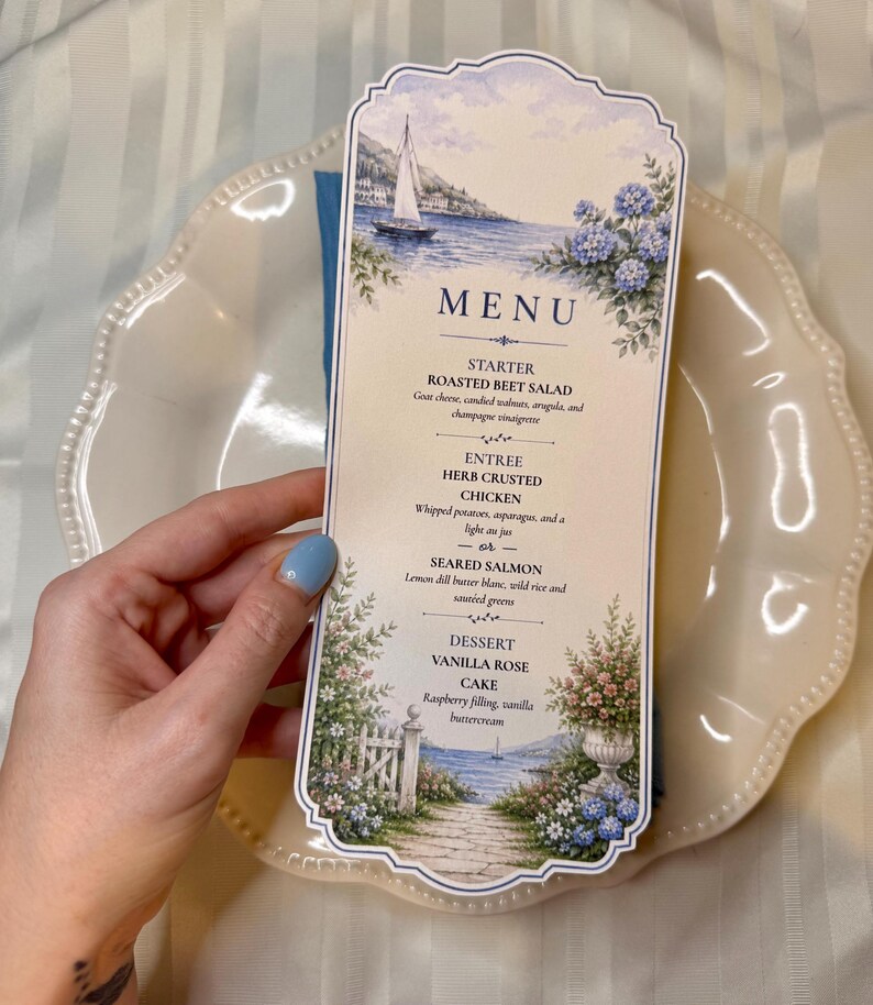 May include: A tall, scalloped-edge menu card featuring a coastal illustration with a sailboat, blue hydrangeas, and a garden path. The text lists a starter of roasted beet salad, entrees of herb crusted chicken or seared salmon, and a vanilla rose cake dessert.