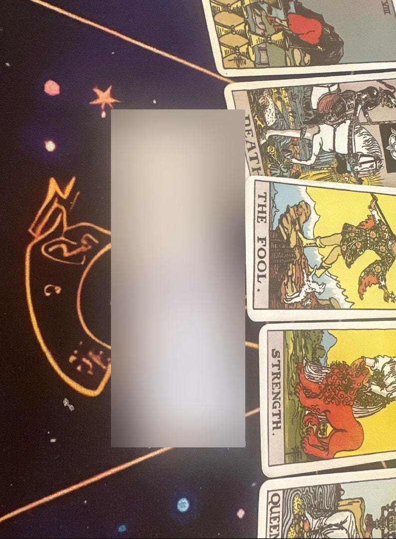 Op de afbeelding: Tarotkaarten met verschillende illustraties en titels, waaronder "Death", "The Fool" en "Strength". De kaarten zijn gerangschikt op een donker oppervlak met een hemels patroon. Een wazig rechthoekig object staat in het midden.
