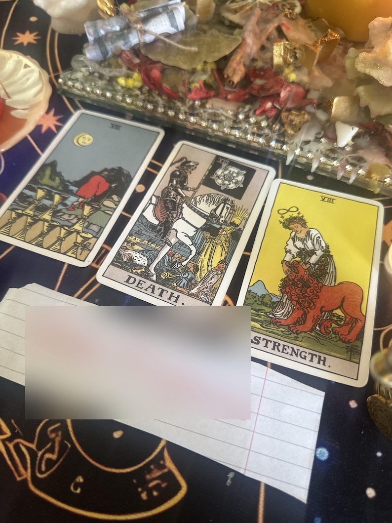 May include: Three tarot cards arranged on a dark surface. The left card shows a figure walking away from eight cups. The center card, labeled DEATH, depicts a skeleton on a white horse. The right card, labeled STRENGTH, shows a person with a lion.