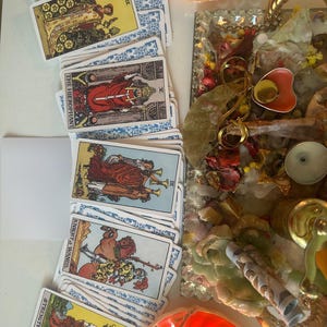 Puede incluir: Una colecci&oacute;n de cartas del tarot con dorsos estampados en azul y blanco, que presentan diversas ilustraciones. Las cartas est&aacute;n dispuestas cerca de una bandeja decorativa con flores secas, una vela y otros objetos espirituales. Las cartas incluyen "El Hierofante" y "Fuerza".