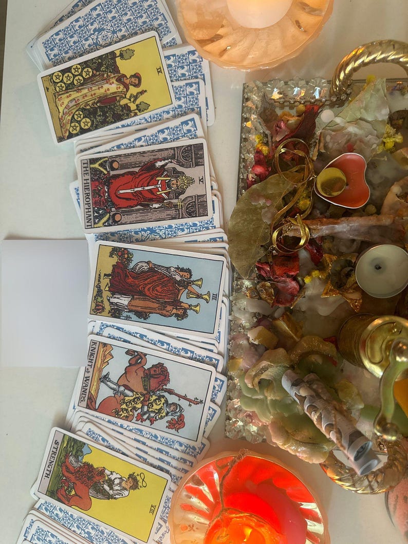 Puede incluir: Una colecci&oacute;n de cartas del tarot con dorsos estampados en azul y blanco, que presentan diversas ilustraciones. Las cartas est&aacute;n dispuestas cerca de una bandeja decorativa con flores secas, una vela y otros objetos espirituales. Las cartas incluyen "El Hierofante" y "Fuerza".
