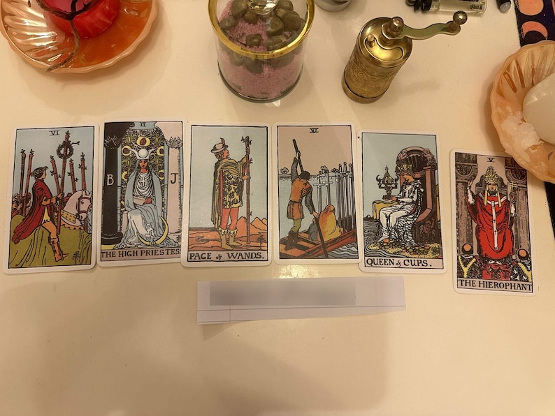 May include: A spread of six tarot cards arranged horizontally, featuring the Six of Wands, The High Priestess, Page of Wands, Six of Swords, Queen of Cups, and The Hierophant. Each card displays detailed illustrations with vibrant colors and text.