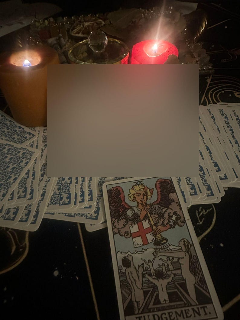 Op de afbeelding: Een tarotkaart met het woord "JUDGEMENT" onderaan, met een engel die op een trompet blaast. De kaart wordt omringd door andere tarotkaarten, brandende kaarsen en decoratieve items, wat een mystieke sfeer cre&euml;ert.