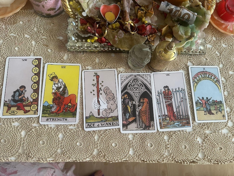 May include: A set of six tarot cards arranged in a row, including the Eight of Pentacles, Strength, Ace of Wands, Three of Pentacles, Eight of Swords, and Ten of Cups, featuring various illustrations of figures, symbols, and landscapes.