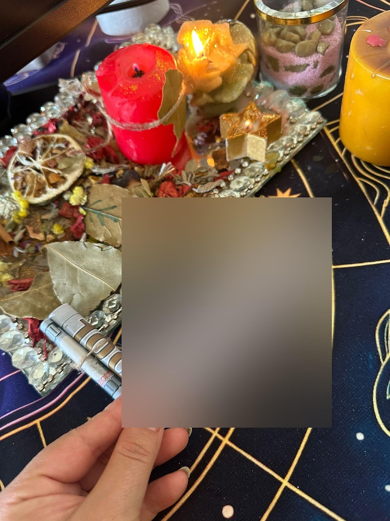 Op de afbeelding: Een verzameling spirituele items, waaronder brandende kaarsen in rode, gele en groene tinten, gerangschikt op een decoratief dienblad. De lade is versierd met gedroogde bloemen en bladeren. Een klein glazen potje met roze korrels en een goudkleurige kaars zijn ook zichtbaar.