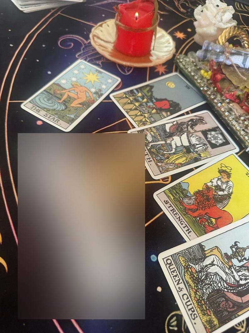 Op de afbeelding: Een verzameling tarotkaarten, waaronder "De Ster", "Kracht" en "Koningin van Bekers", ligt op een donkere, bedrukte doek. Een brandende rode kaars en een decoratief dienblad zijn ook zichtbaar.