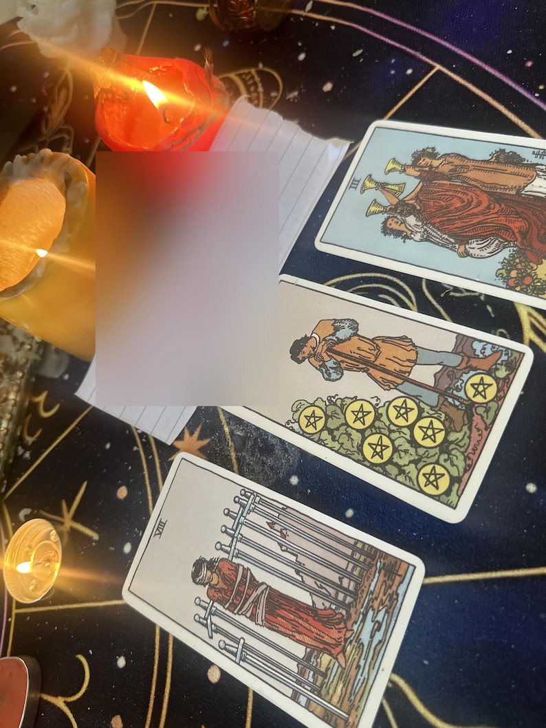 May include: Three tarot cards arranged on a dark surface with gold celestial patterns. The cards include the Three of Cups, the Seven of Pentacles, and the Eight of Swords. Two lit candles with orange and yellow flames are positioned nearby.