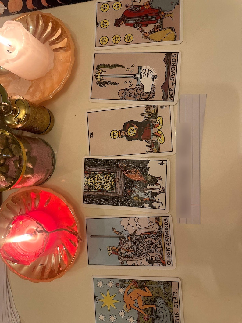 May include: A vertical arrangement of six tarot cards including the Six of Pentacles, Ace of Swords, Four of Pentacles, Five of Pentacles, Queen of Swords, and The Star. To the left are two lit candles in gold-toned holders and a glass jar with pink sand.