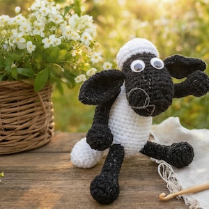 May include: A handmade crochet sheep toy with a white body, black legs, and a black head with googly eyes. The sheep is sitting on a wooden surface next to a basket of white flowers and a ball of yarn. A crochet hook is also visible.