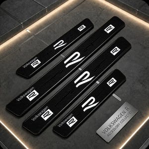 Könnte beinhalten: Vier schwarze, rechteckige Türschwellenschutzleisten mit Carbonfaser-Struktur. Jedes Teil zeigt den weißen Volkswagen-Schriftzug und das R-Logo. Eine kleine rechteckige Metallplakette trägt den Text VOLKSWAGEN R ACCESSORY COLLECTION.