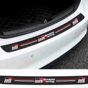 May include: Black carbon fibre bumper protector with red and white accents. Features "GR Sport" and "Gazoo Racing" logos. Designed to protect the bumper from scratches. Automotive accessory.
