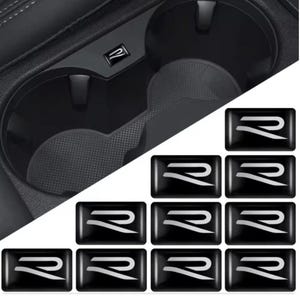 May include: A set of eleven rectangular black adhesive emblems featuring a silver stylized letter R. One emblem is shown applied to the interior of a black plastic vehicle cup holder, while the remaining ten are arranged in a grid below.