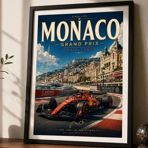 Può includere: Poster incorniciato raffigurante il Gran Premio di Monaco. L'immagine mostra un'auto di Formula 1 rossa su un circuito, con la città e il mare sullo sfondo. Il poster presenta le parole "MONACO GRAND PRIX" in stile vintage.