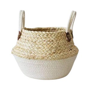 May include: A two-toned storage basket featuring a natural tan woven straw upper section and a solid off-white cotton rope base. The basket includes two upright off-white handles attached with small dark brown leather-like triangular accents.