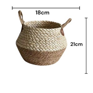May include: A round woven basket featuring a two-tone design with a light beige upper section and a darker brown lower section. The basket includes two side handles and is marked with dimensions of 18 cm in width and 21 cm in height.