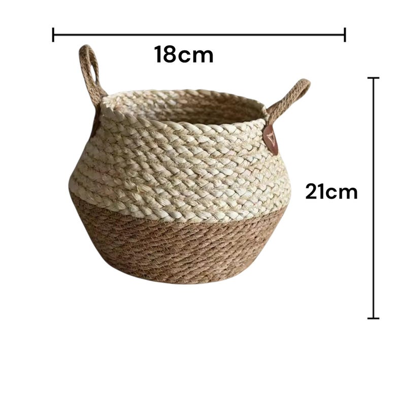 May include: A round woven basket featuring a two-tone design with a light beige upper section and a darker brown lower section. The basket includes two side handles and is marked with dimensions of 18 cm in width and 21 cm in height.