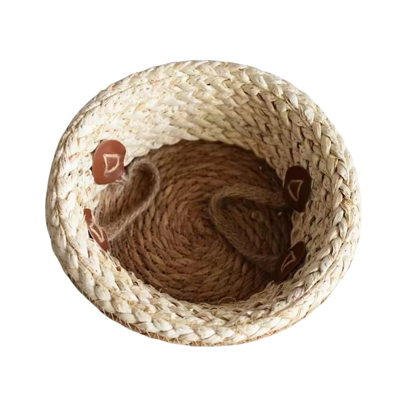 May include: A round woven basket featuring a light beige braided rim and a dark brown coiled base. The interior walls are accented with four small, circular brown leather-like patches, each embossed with a simple triangular geometric symbol.