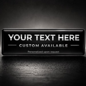 May include: A rectangular black name badge with rounded corners. The text "YOUR TEXT HERE" is in white, with "CUSTOM AVAILABLE" below. The phrase "Personalized upon request" is at the bottom.