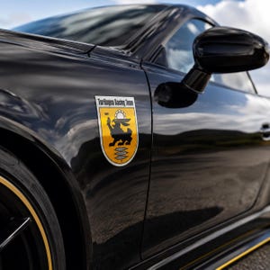 May include: A glossy black car featuring a Terlingua Racing Team decal on the front fender. The shield-shaped emblem displays a black rabbit silhouette, a sun graphic, and three feathers on a yellow background with the text Terlingua Racing Team.