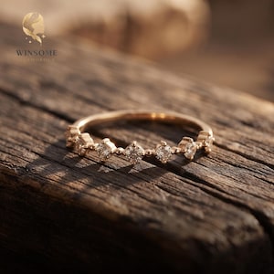 May include: A gold ring featuring a series of small, round, clear stones set along the band, interspersed with tiny gold beads. The band has a polished finish and the stones are arranged in a row. The text WINSOME GLAMOROUS is visible.