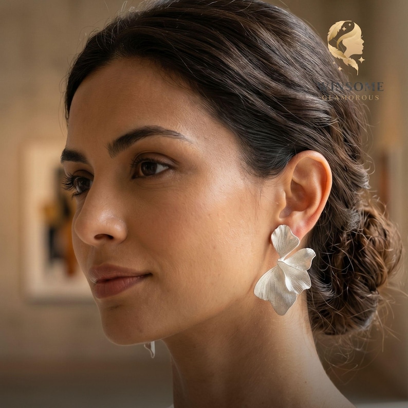 May include: A silver-toned earring shaped like a delicate, multi-layered flower petal with a matte finish. The earring features organic, flowing curves that mimic the appearance of a natural leaf or blossom, attached to the earlobe.