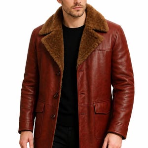 May include: A long, rust-colored leather coat featuring a wide, brown shearling collar and lapels. The coat includes a button-front closure, two large flap pockets at the hips, and long sleeves, worn over a simple black sweater.