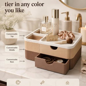 May include: A beige and brown multi-tiered cosmetic organiser with drawers and compartments. The top tier holds bottles and accessories. Text reads: "Customize each tier in any colour you like." The middle and base are drawers. Stylish organisation.