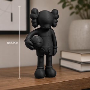 May include: A matte black figurine of a character with X-shaped eyes and crossbones-style ears, holding a basketball under one arm. The figure features visible stitched seam details across its body and stands at a height of 10 inches.