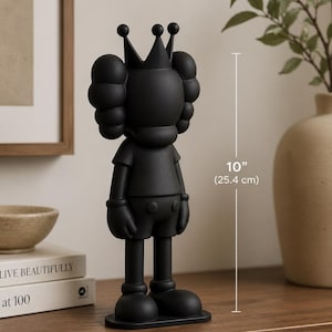 May include: A black figurine of a cartoon character wearing a crown, standing on a rectangular base. The figurine is 25.4 cm tall. The character has large, rounded ears and gloved hands. The figurine is displayed on a wooden surface.