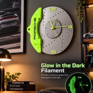 May include: A wall clock designed as a silver brake rotor with a bright green brake caliper featuring the text PORSCHE. The clock has green hands and green numbers 12, 3, and 6. A small inset shows the clock glowing in the dark.