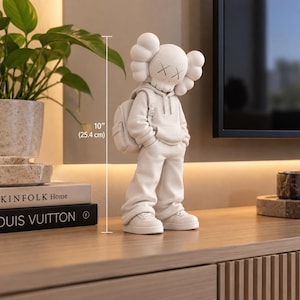 May include: A matte white collectible figure featuring a character with X-shaped eyes, wearing a hooded sweatshirt, loose pants, sneakers, and a backpack. The figure stands 10 inches tall, as indicated by the visible measurement marker.
