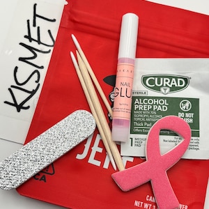 May include: A nail care kit containing a red pouch labeled KISMET, a silver glitter nail file, two wooden cuticle sticks, a tube of Makartt nail glue, a Curad alcohol prep pad, and a pink foam ribbon-shaped nail buffer on a red background.