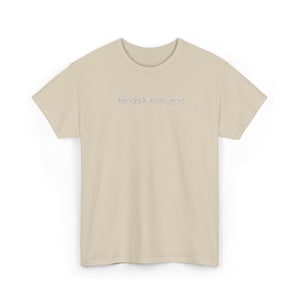 以下が含まれることがあります： ベージュ色のTシャツ。胸には「Jesus loves you」の文字が薄いグレーでプリントされています。半袖で、クルーネックです。