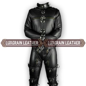 Op de afbeelding: Zwarte leren jas en broek set met meerdere metalen ringen, ritsen en gespen. De jas heeft een hoge kraag en lange mouwen. De broek heeft riemen en zakken. De tekst "LUXGRAIN LEATHER" wordt op de afbeelding weergegeven.