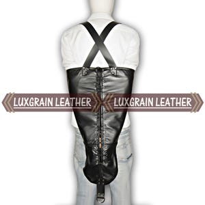 Może przedstawiać: Czarny skórzany kaftan bezpieczeństwa z wiązanymi plecami i ramiączkami. Produkt posiada D-ring na dole oraz napis "LUXGRAIN LEATHER" z boku.