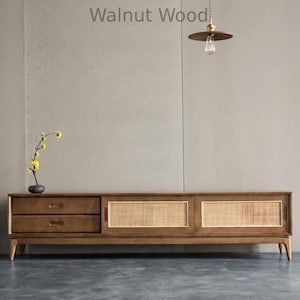 Puede incluir: Consola de medios de madera de nogal de estilo moderno de mediados de siglo con dos cajones y dos puertas correderas con inserciones de caña tejida. El texto "Walnut Wood" es visible.