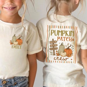 May include: A natural-colored t-shirt featuring a small pumpkin graphic and the name Emily on the front left chest. The back displays a large graphic with pumpkins, a wooden sign reading Fun Fall Memories, and the text Pumpkin Patch Crew.