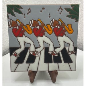 May include: A square ceramic tile featuring a repeating illustration of three musicians in red jackets and white trousers playing yellow saxophones. The figures stand on a black and white piano key pattern against a gray background with green palm leaves.