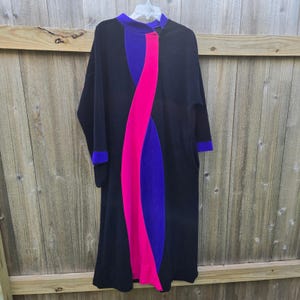 May include: A long-sleeved black dress featuring a high neckline and a prominent, vertical, wavy color-blocked design down the center. The pattern consists of a bright hot pink stripe flanked by deep purple panels, with matching purple sleeve cuffs.