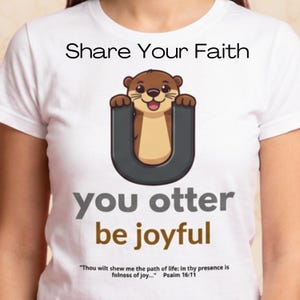 May include: White t-shirt with the text "Share Your Faith." The shirt features a cartoon otter inside a grey "U" shape, with the words "you otter be joyful." A Bible verse is printed below.