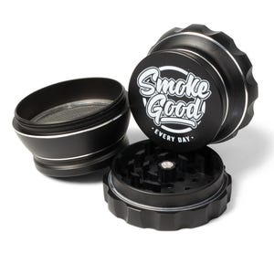 May include: Black grinder with the text "Smoke Good EVERY DAY" in white script. The grinder is disassembled, showing the different parts, including a mesh screen and a grinding chamber. The grinder has a silver trim.