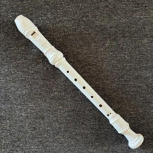 May include: A white plastic recorder musical instrument featuring a mouthpiece at the top, a central body with a series of circular finger holes arranged in a straight line, and a flared bell at the bottom end, showing a smooth matte finish.