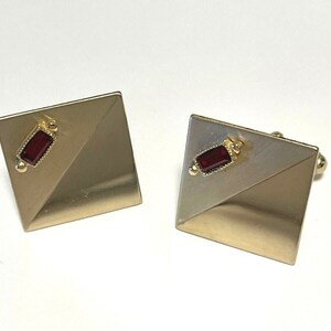 May include: A pair of gold cufflinks with a red rectangular stone set in each. The cufflinks have a geometric design with a diagonal line.