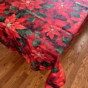 May include: Red tablecloth with a poinsettia print. The tablecloth is made of a linen blend and features a festive holiday design.