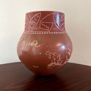 May include: A red clay pottery vase with a white geometric design. The vase has a rounded body and a wide mouth.