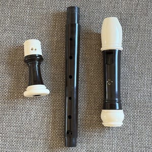 May include: A disassembled dark brown and white recorder musical instrument consisting of three separate parts. The head joint features a white mouthpiece, the middle section has finger holes, and the foot joint has a white flared end piece.